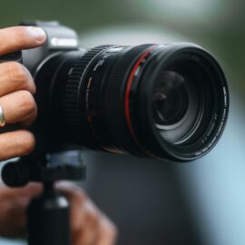 Detailed close-up of a DSLR camera with lens on a tripod held by a person.