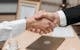 Close-up of two people shaking hands in an office, symbolizing agreement and partnership.