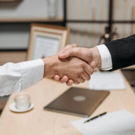 Close-up of two people shaking hands in an office, symbolizing agreement and partnership.